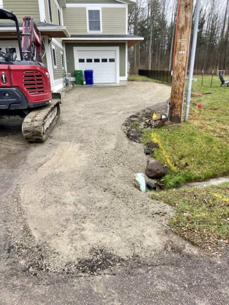A driveway that has been installed by Firebrick Masonry and Excavation with an excavator parked on it.
